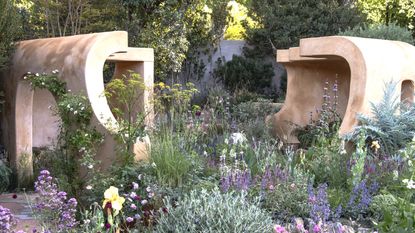 A large, wild flower bed with salvias, iris, dill, and a terracotta structure in the background