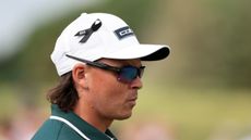 A side view of Rickie Fowler's head where he's wearing a white cap and black ribbon with 'KH' inscribed on