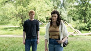 Domhnall Gleeson in a dark top and jeans as Jack and Aisling Bea in a striped top, white cardigan and jeans as Lynn stand together in a wooded area in Alice & Jack
