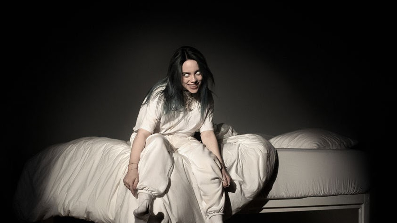 Η Billie Eilish κάθεται σε ένα κρεβάτι ντυμένη στα λευκά