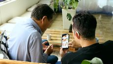 A senior man and his son order food on their phone while sitting on a couch.