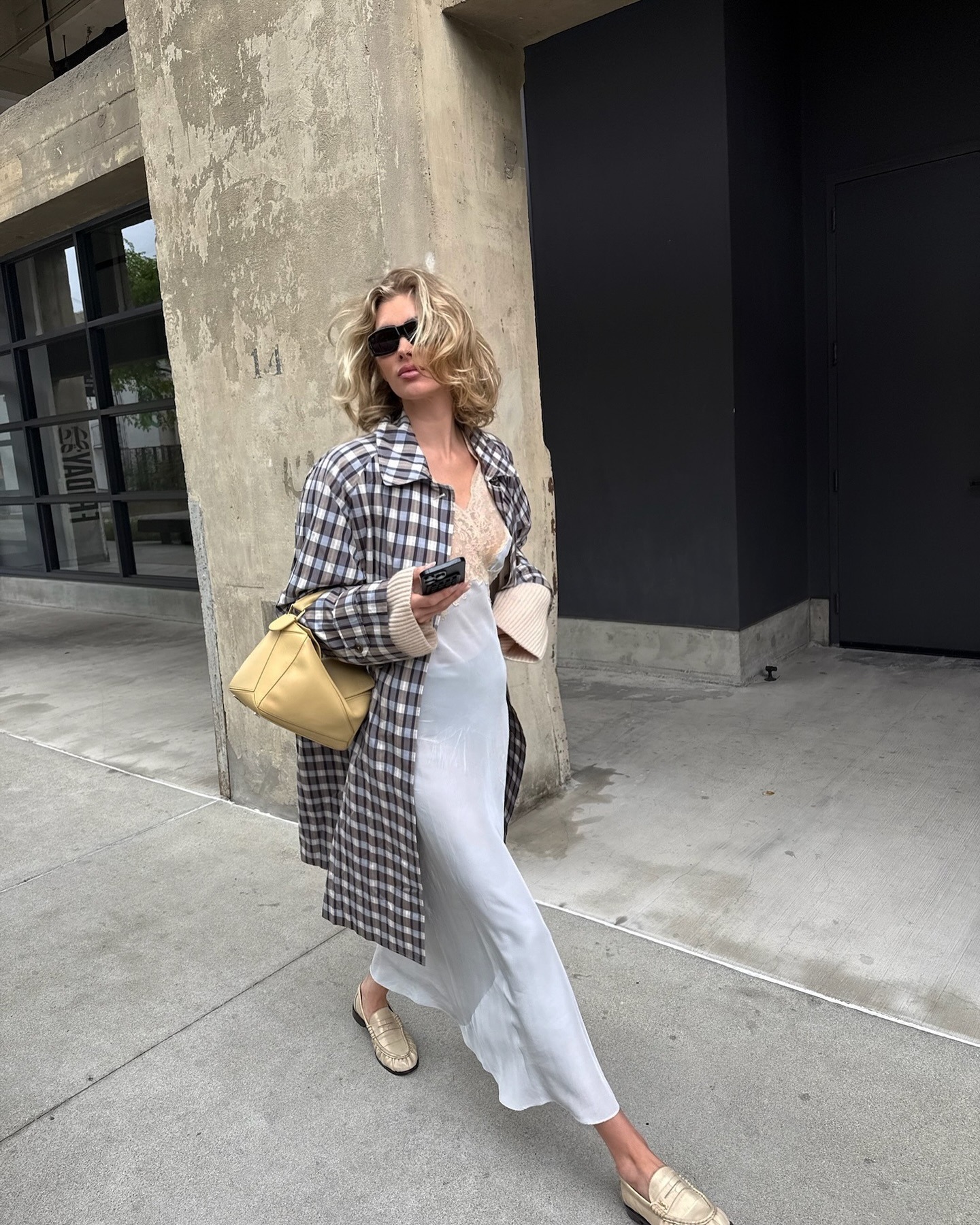 Elsa Hosk wearing a checked The Row trench coat, white slip dress, and loafers