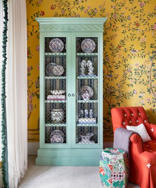 yellow floral wallpaper in a living room with a large antique dresser filled with china