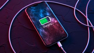 Mobile smart phone on wireless charging device on dark neon red and blue color background. Icon battery and charging progress lighting on screen.