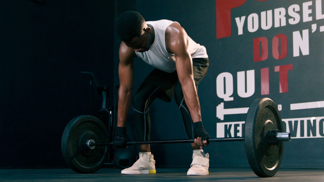 Man doing floating deadlifts in a gym with barbell and weight plates