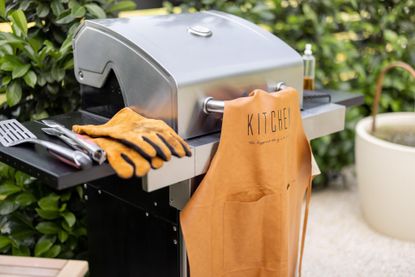 A gas grill with accessories including an apron and gloves