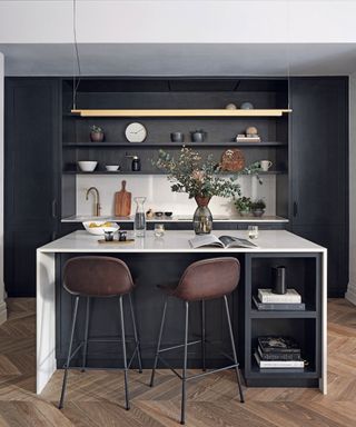Kitchen with wooden flooring, black and cream fitted units, bar stools by the breakfast bar, high ceilings and coving.