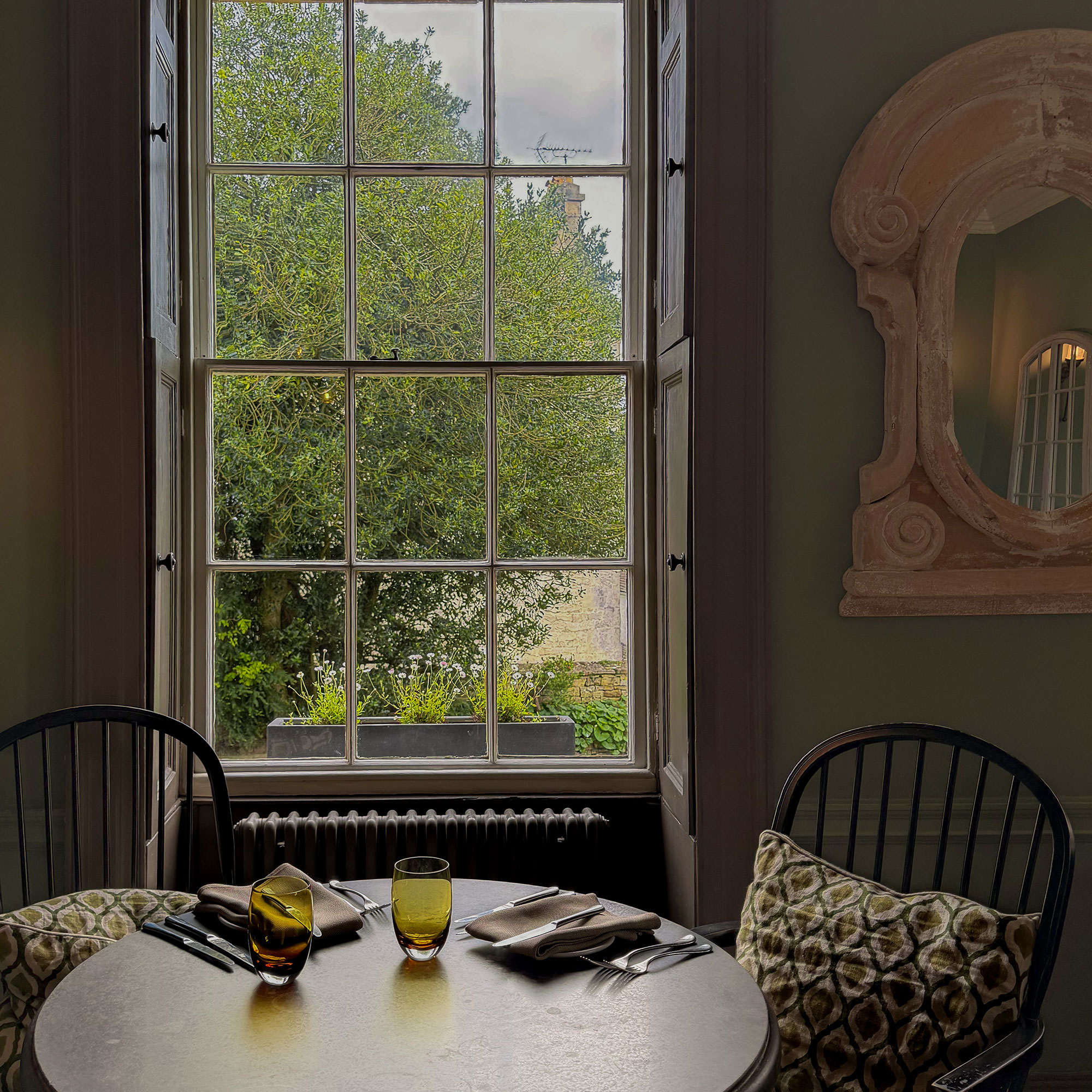Wooden table with two dining chairs and place settings in front of window
