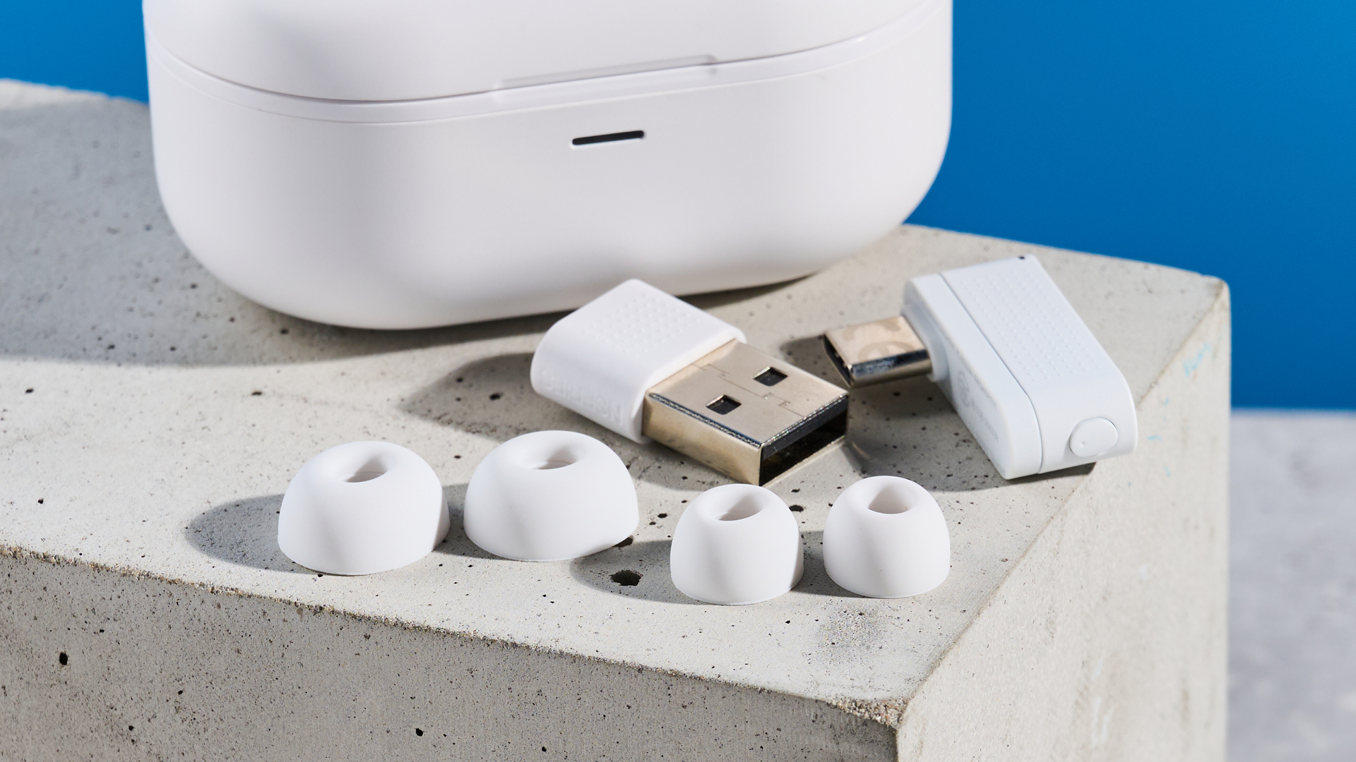 the akg n5 hybrid earbuds by harman in white, shown in their charging case with accessories and without