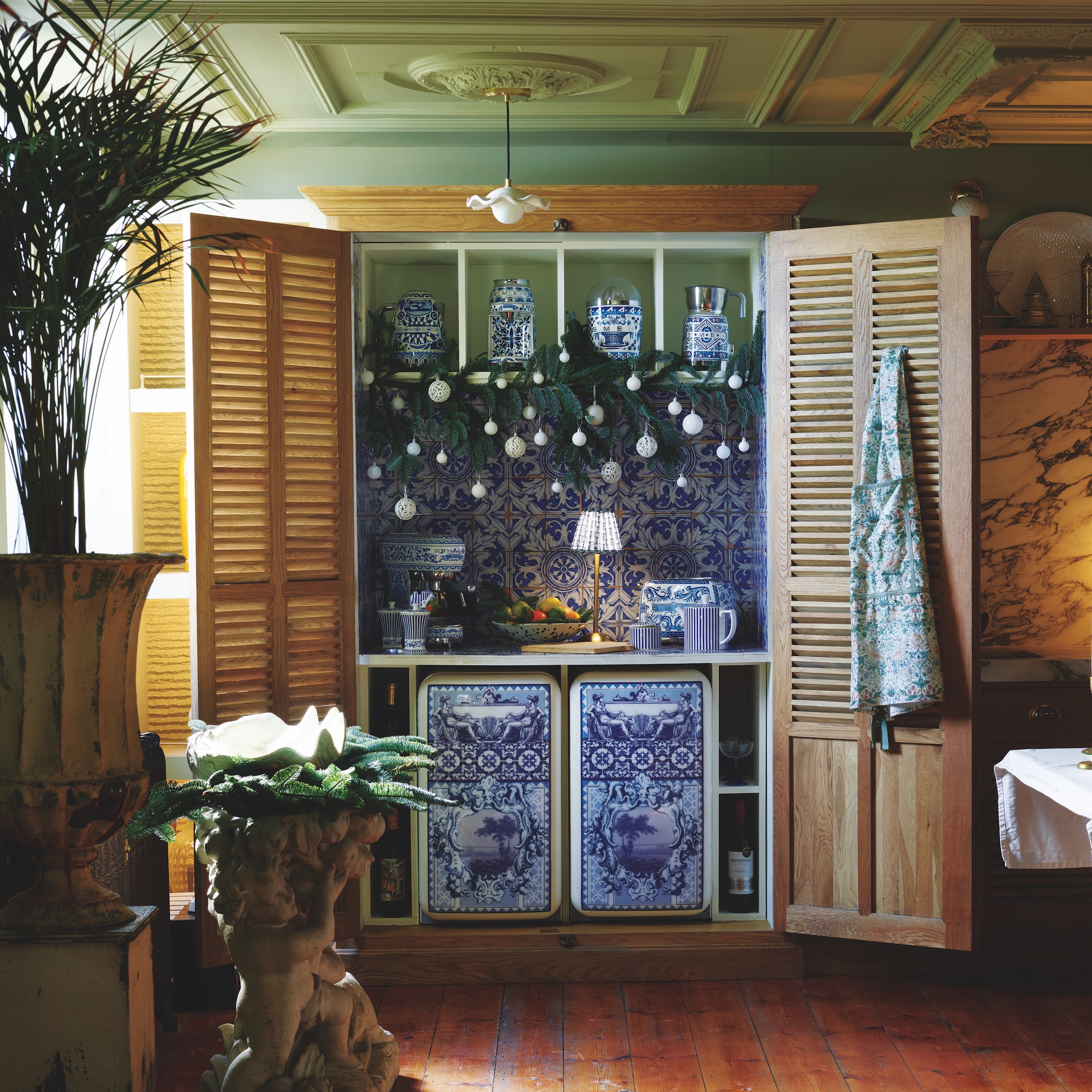 cupboard with louvre doors in kitchen containing smeg dolce gabbana fridge and freezer with blue and white porcelain wall tiles