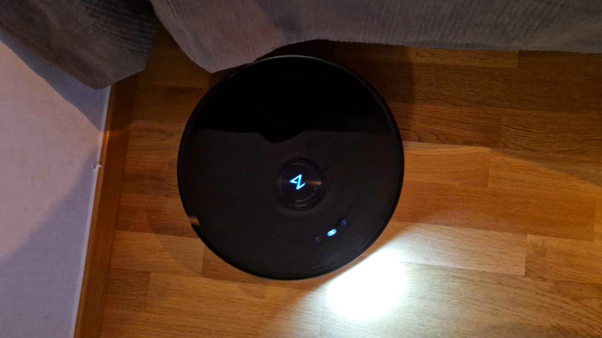Roborock S8 MaxV Ultra valaisemassa puulattiaa pimeässä huoneessa