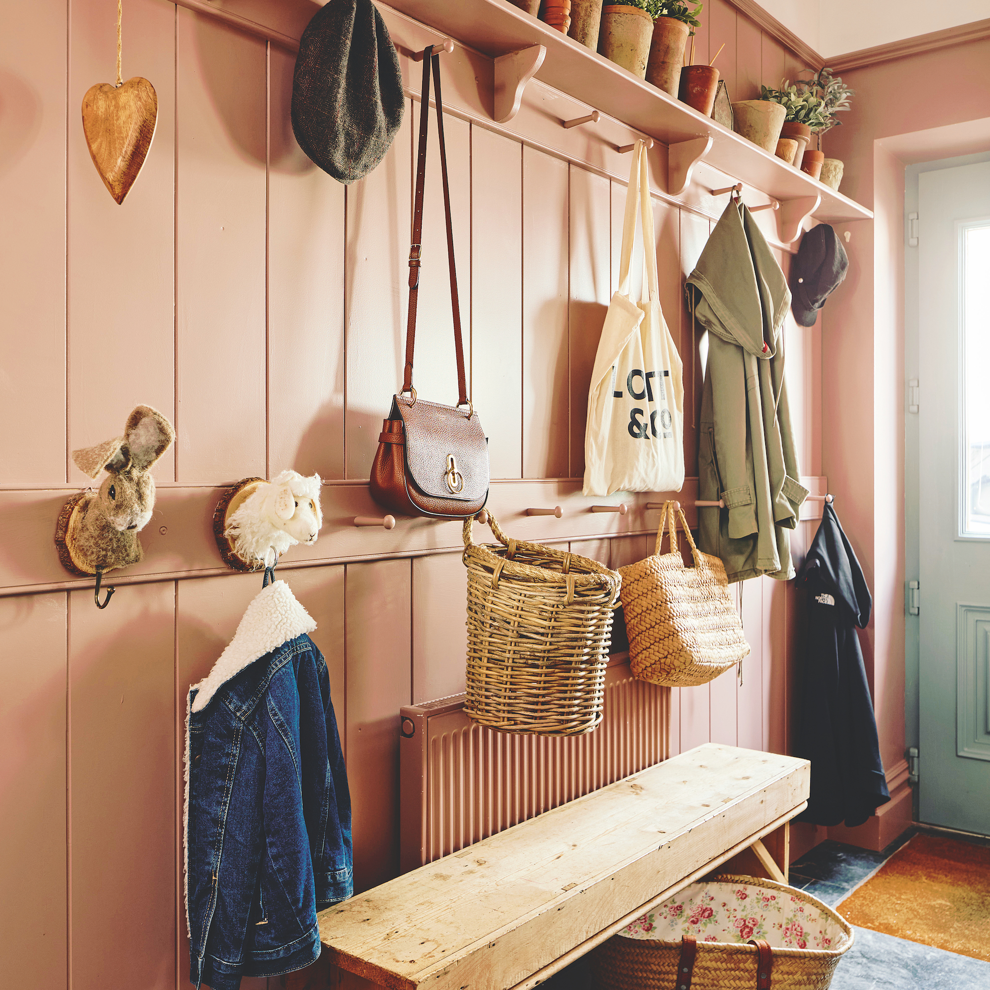 boot room with wood panel walls painted pink with hooks and shelves for bags and flowerpots