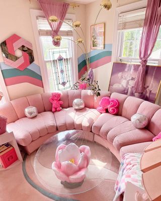 A pink living room with a pink corner sofa and glass table