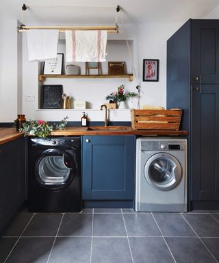 A laundry room with navy blue cabinetry, washing machine and recess with framed art and home furnishings
