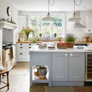 country kitchen with pale blue island unit, white wall units and range cooker in fireplace