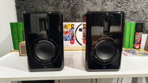 Quad Revela 1 standmounted speakers side by side on white shelf with books behind them