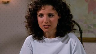 Julia Louis-Dreyfus as Elaine, sitting in a doctor's office in a hospital gown