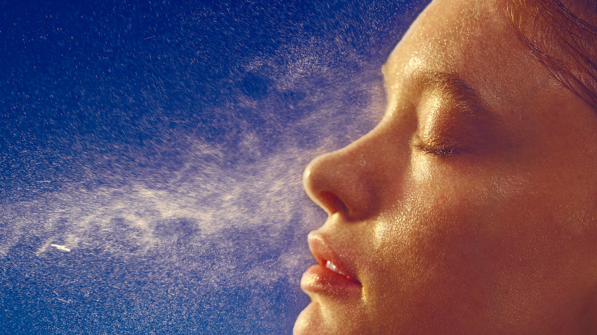 best face mists - image of a woman spraying a mist onto her face side on - gettyimages 1785634303