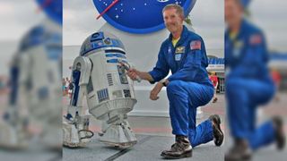 Astronaut Jim Reilly poses with Luke Skywalker's lightsaber and R2D2 before taking the famous prop into space.