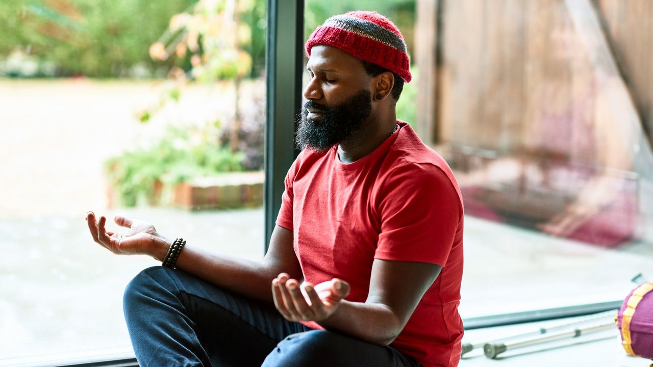 Wrist-free yoga flow: Image shows mature man wearing hat meditating in yoga class