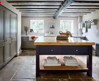 Utility room storage ideas showing a large wooden island and built-in floor to ceiling cabinets and dark wooden ceiling beams