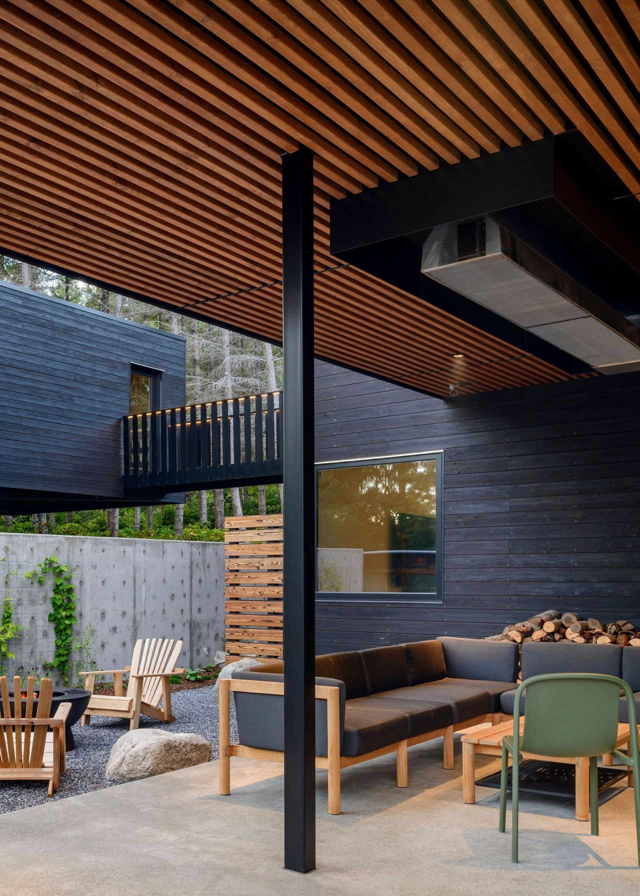 Beneath a pergola is a sofa as well as a coffee table and chairs. Beside the sofa and on the other side are chairs surrounding a firepit.