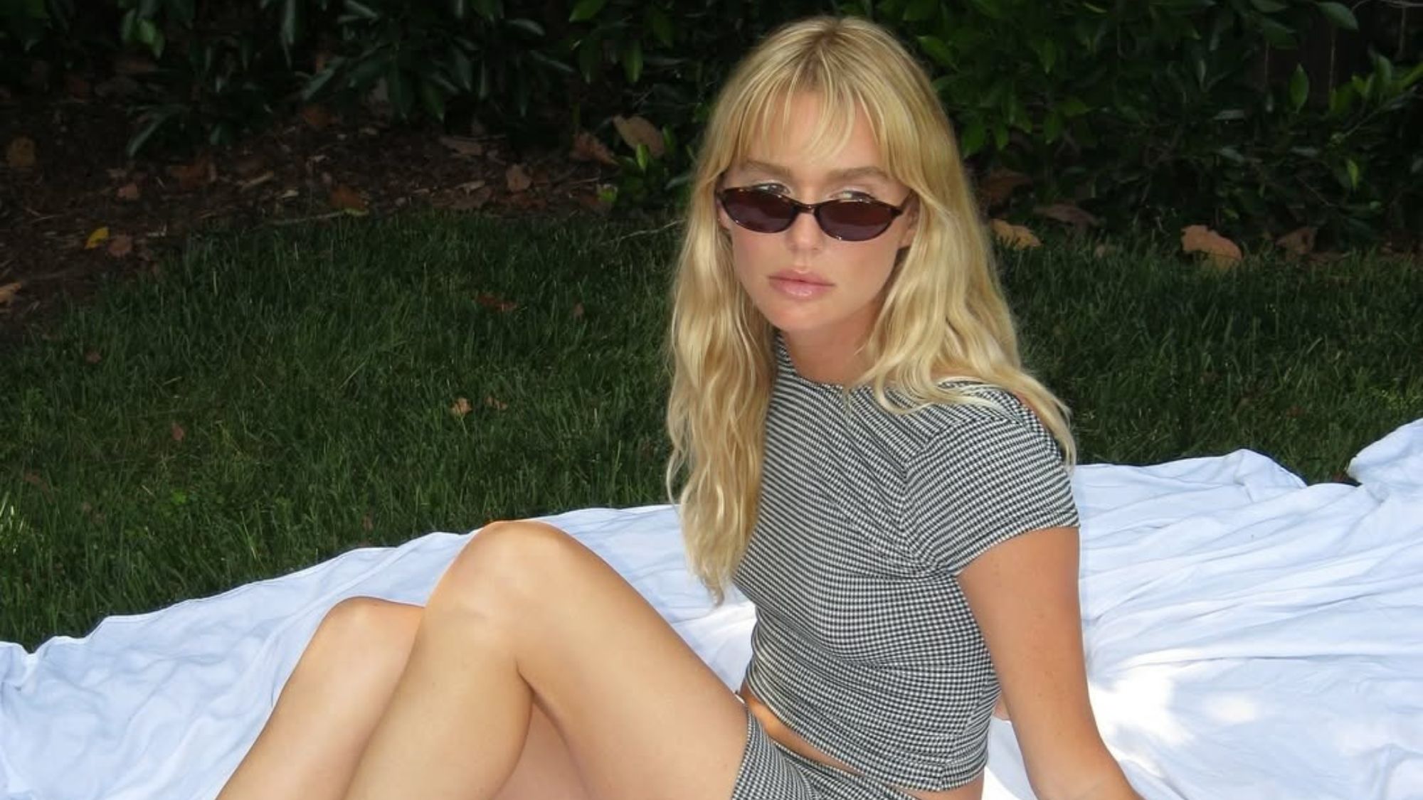 Woman sitting on a picnic blanket wearing sunglasses and beach waves.