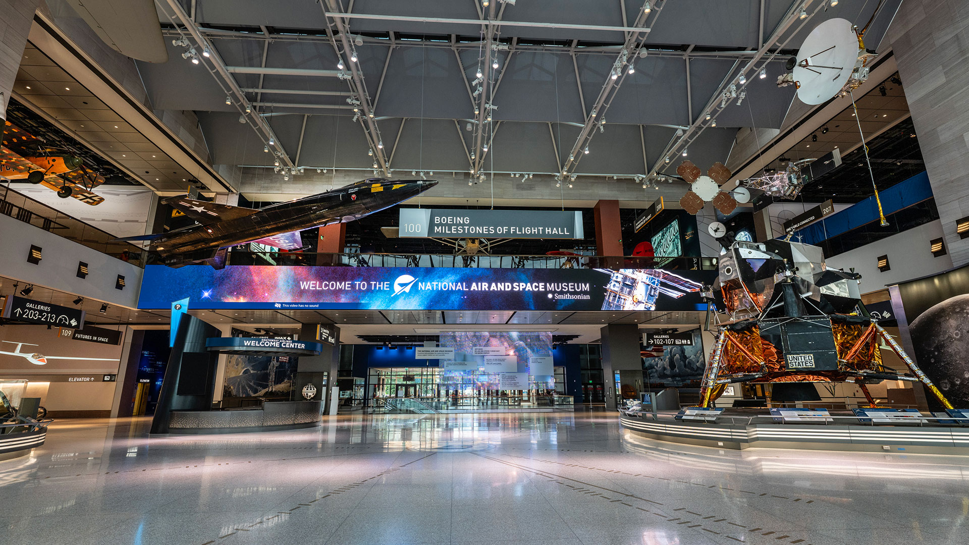 a museum gallery with a wide open space at its center, aircraft suspended from the ceiling and spacecraft standing on the floor