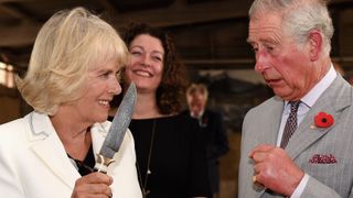 Camilla holds a knife while smiling with Charles
