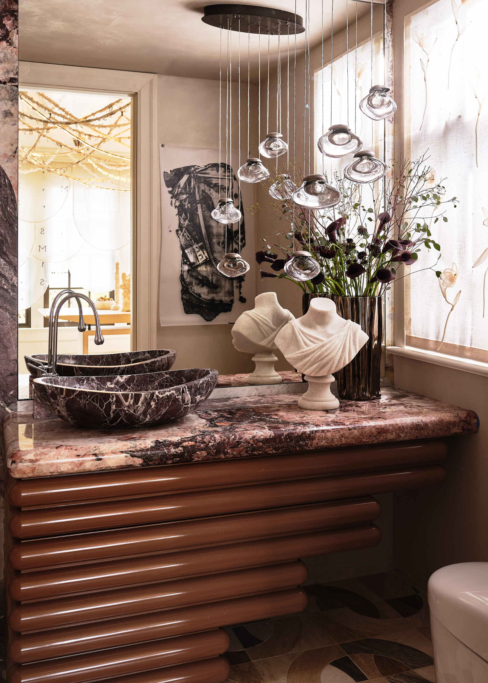 tiered sink vanity with a red marble sink and a plaster bust next to it and a dramatic waterfall light fitting above