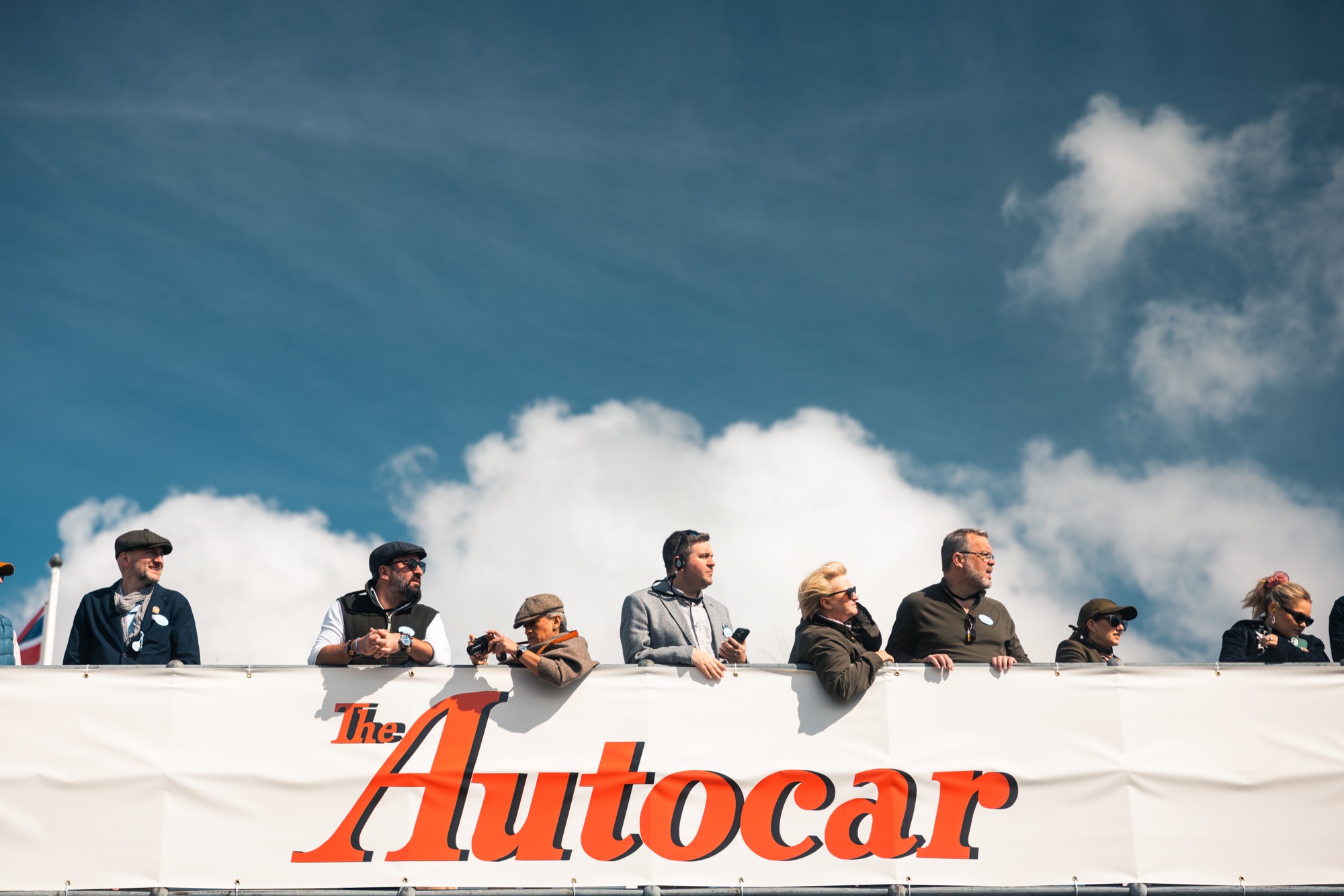 People watch the racing while overlooking an old advert for Autocar