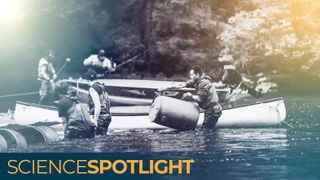 men standing in a river with canoes lift barrels