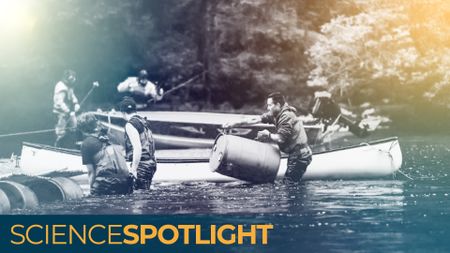 men standing in a river with canoes lift barrels