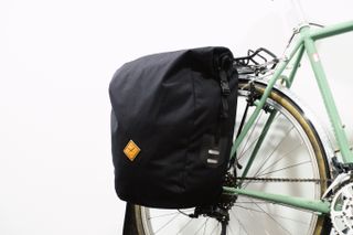 A black canvas rolltop pannier mounted to a green bike against a white background