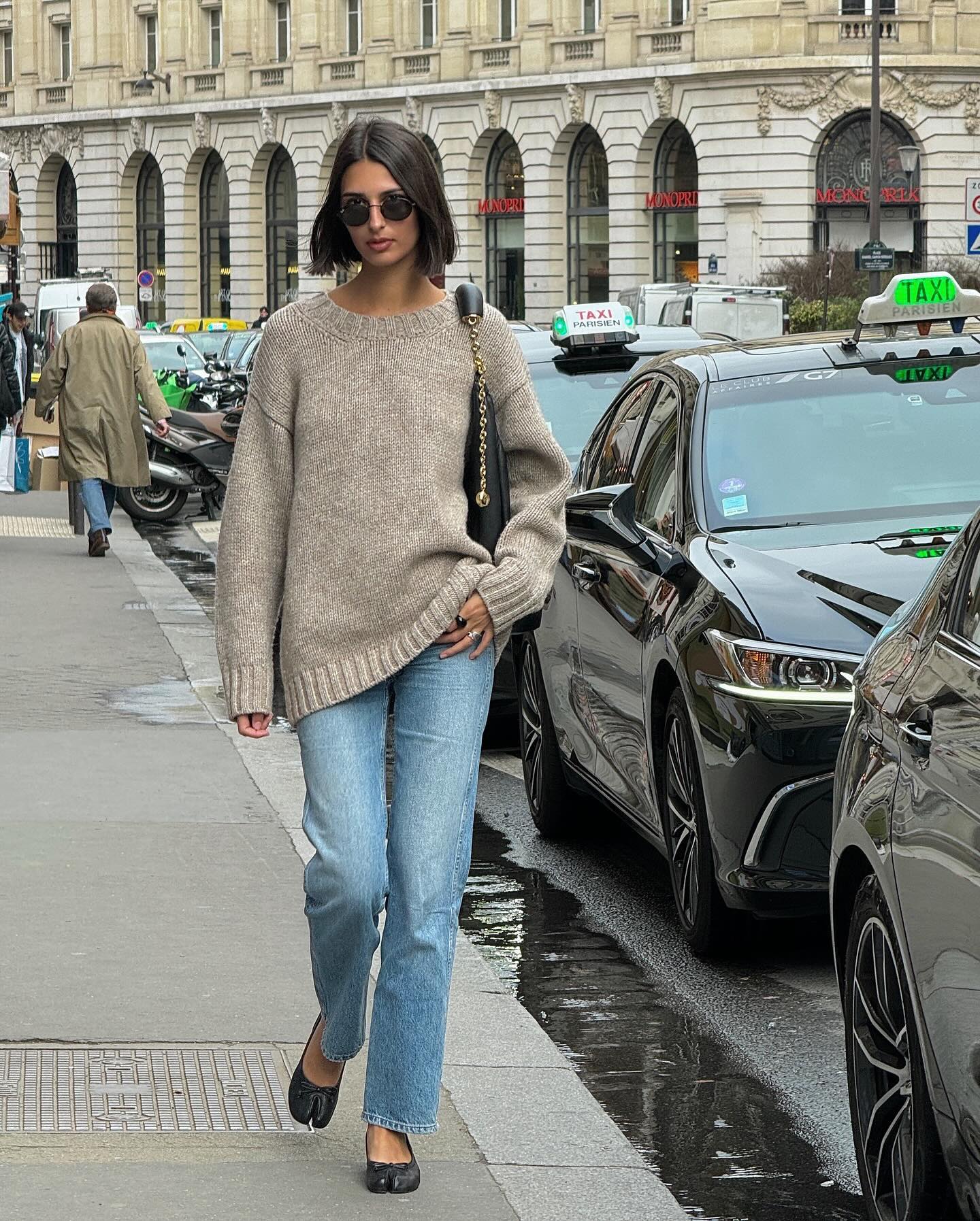 stylish French woman with a bob haircut walking on the sidewalk in Paris wearing an oversized neutral sweater, straight-leg jeans, and black Margiela Tabi ballet flats