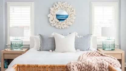 Coastal bedroom ideas are always beautiful. Here is a blue bedroom with a blue wall with white mirror, white bed, rattan bench, and knitted throw