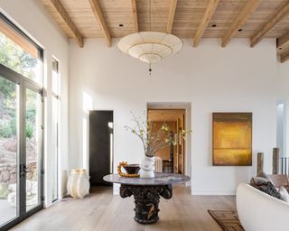 neutral entryway with round coffee table, pendant light, wood ceiling and white walls