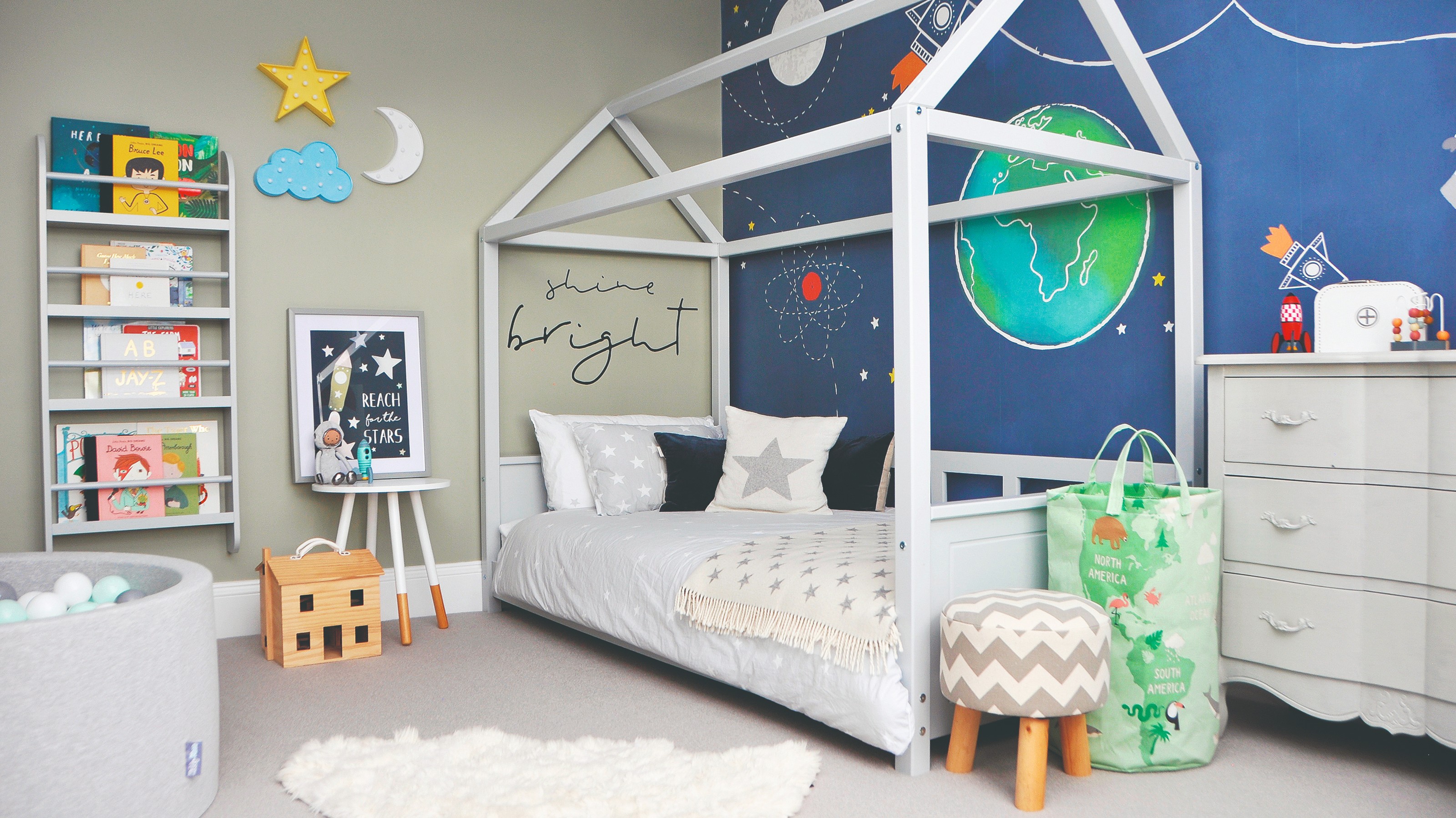 A boy's bedroom with a space-theme wallpaper feature wall and a house-shaped bed