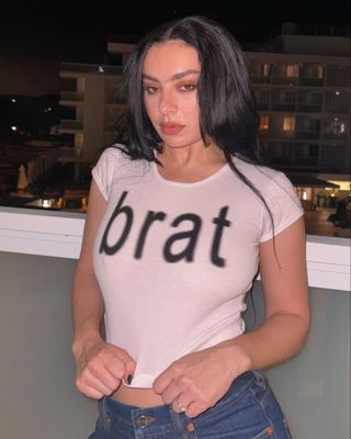 Charli XCX wears a white Brat T-shirt and blue jeans.