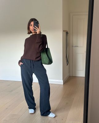 Marianne Smith wears drawstring trousers with a brown sweater, trainers and green The Row bag.