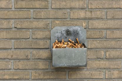 Metal gray ashtray filled with smoked cigarettes