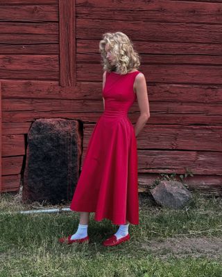 Elsa wears a red midi dress, sock, and red boat shoes.