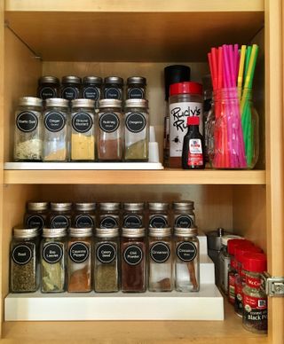 An organised spice cupboard on shelf risers with labelled spice jars