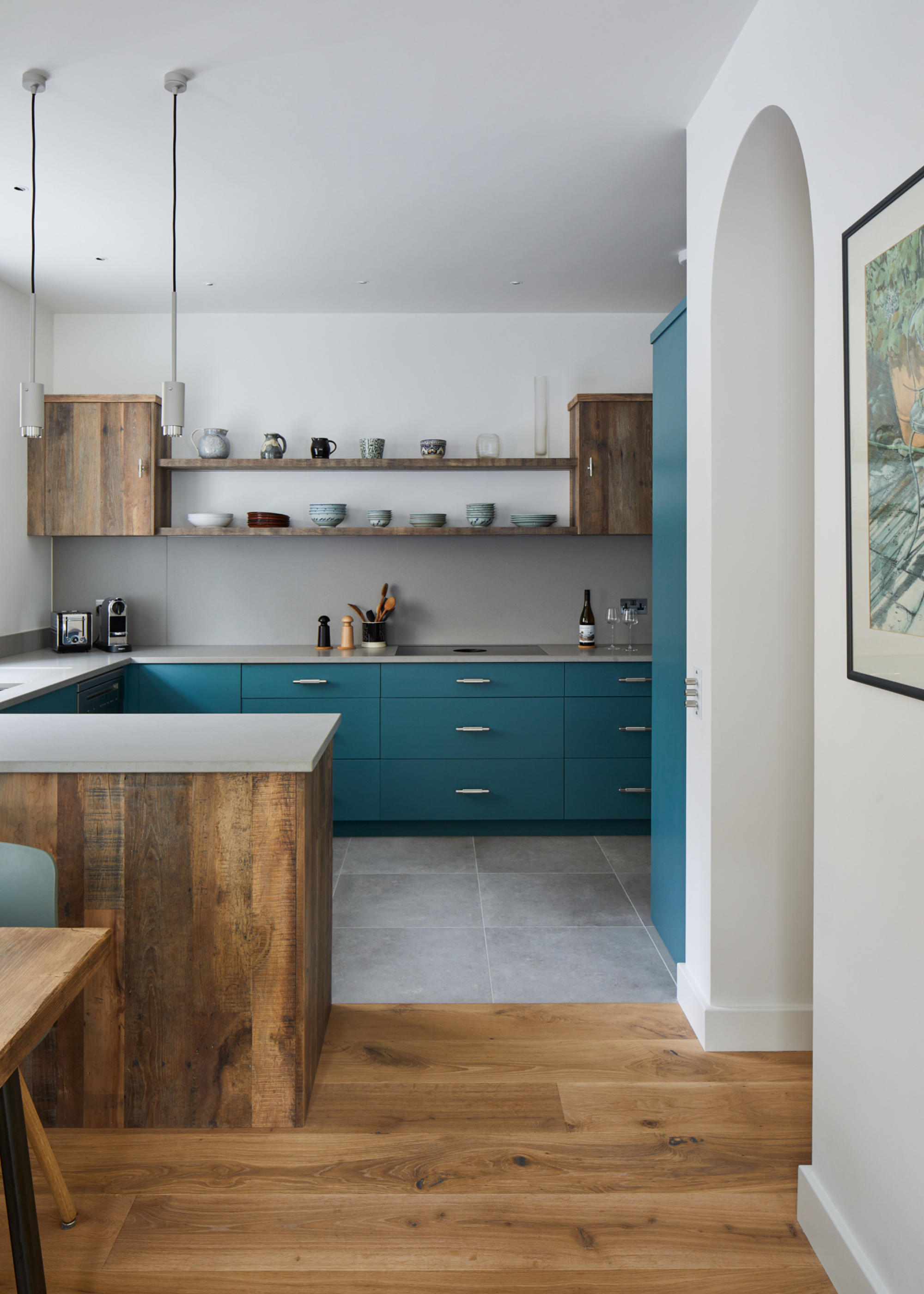 An aqua blue modern kitchen with grey tiles and a peninsula island to separate the dining area which has wooden flooring