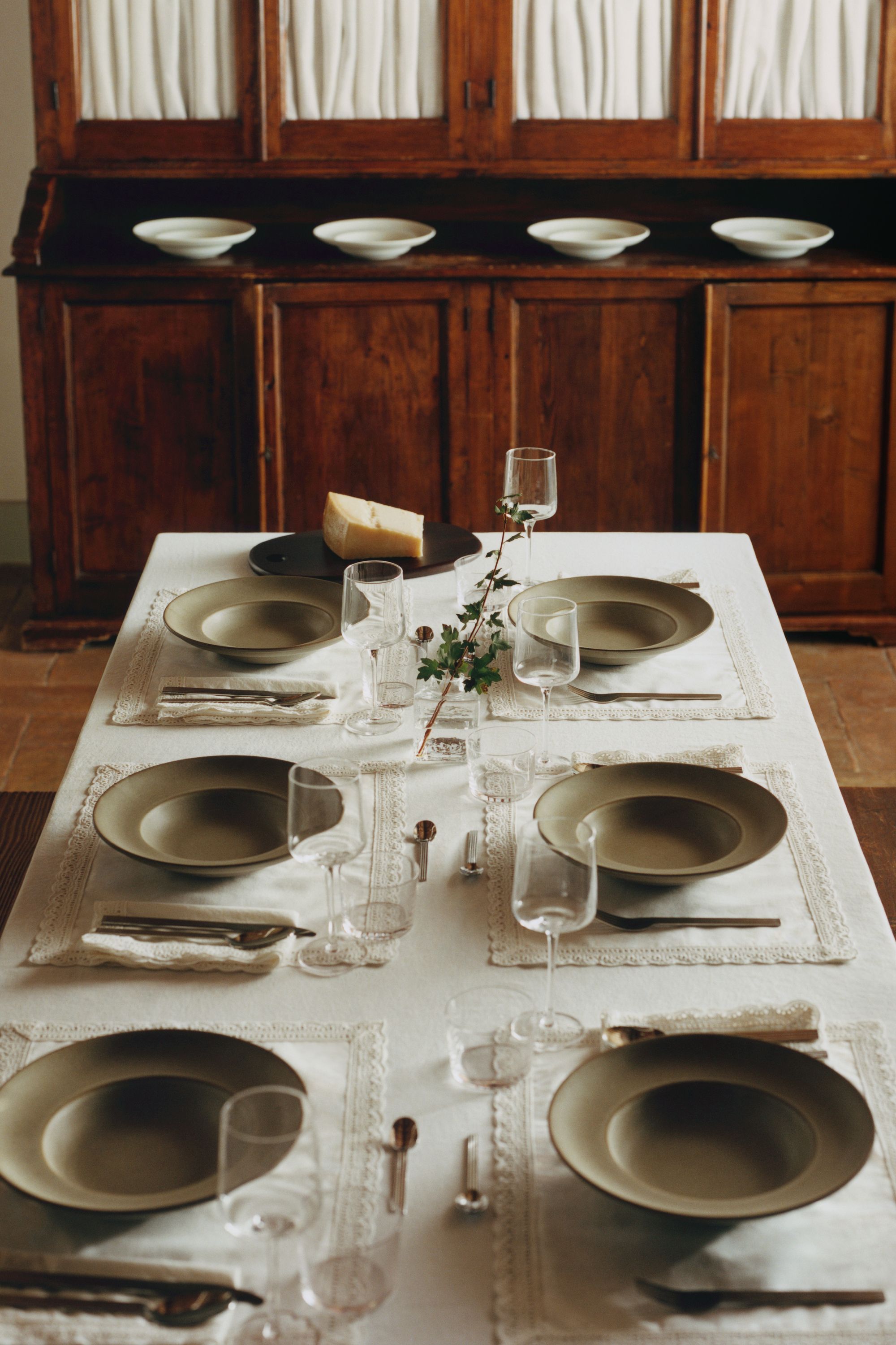 table set with H&amp;M home linen tablecloth and lace-trimmed placemats with brown bowls, glassware, and a timber cabinet in the background