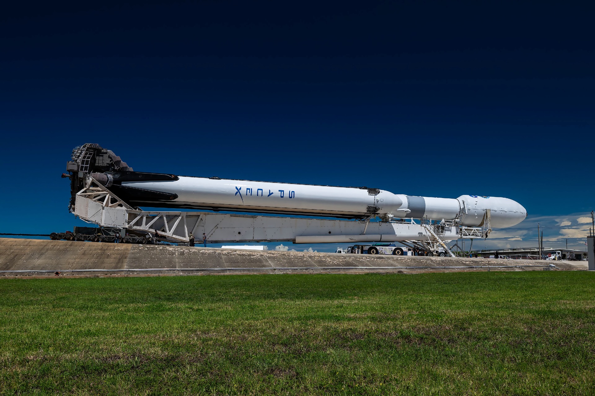 a large white rocket is transported horizontally toward its launch pad, with a blue sky in the background