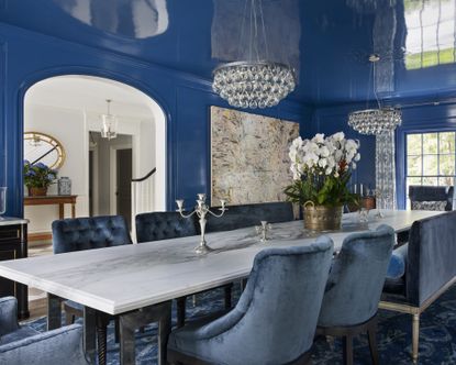 A dining room with blue gloss walls and ceiling and blue velvet chairs 