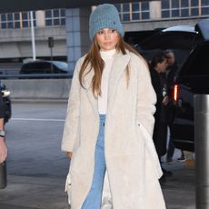 Jennifer Lopez wears a blue beanie, ivory shearling long coat, white turtleneck, and blue flare jeans.