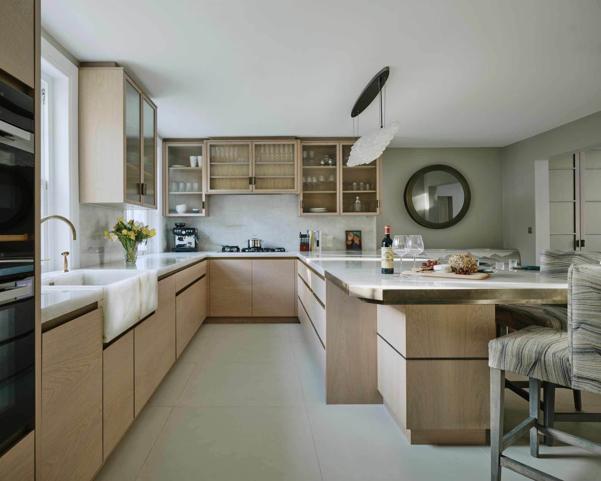 A wooden kitchen with a marble sink and large island with glass cabinetry