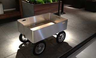 Grey marble style slab floor, silver wagon style outdoor trolley, black and silver wheels, wooden planter in the background